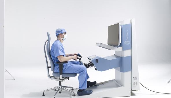 A surgeon sitting in front of a monitor in a white room